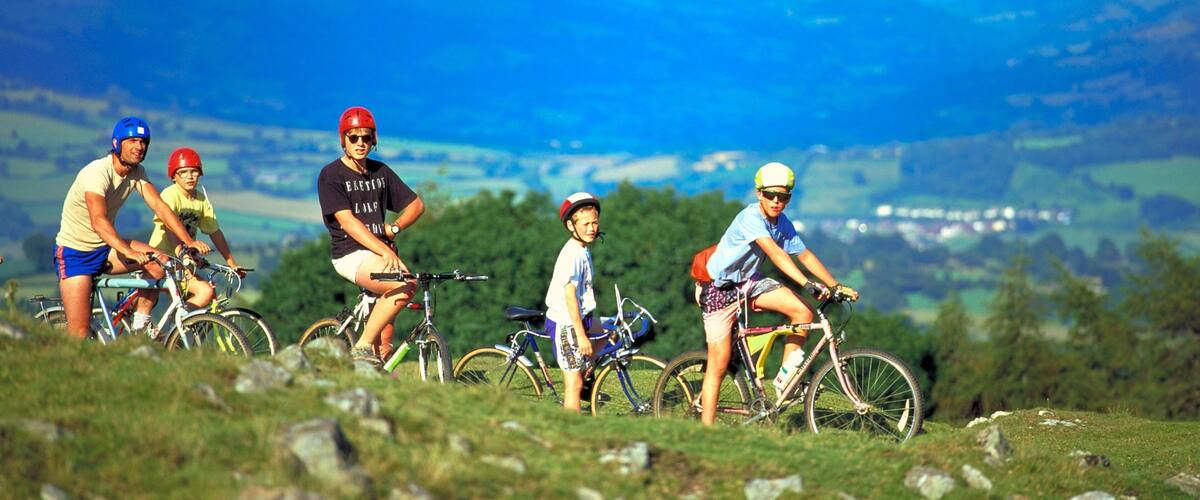 A group of cyclists on a grassy hill with a mountainous landscape in the background.