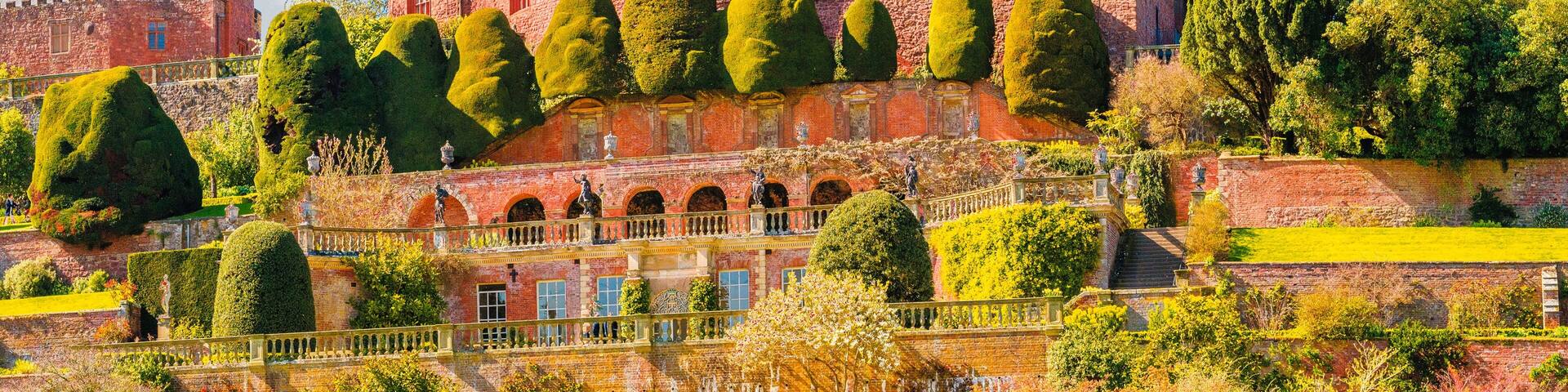 A large red brick castle with multiple towers and a well-maintained garden.