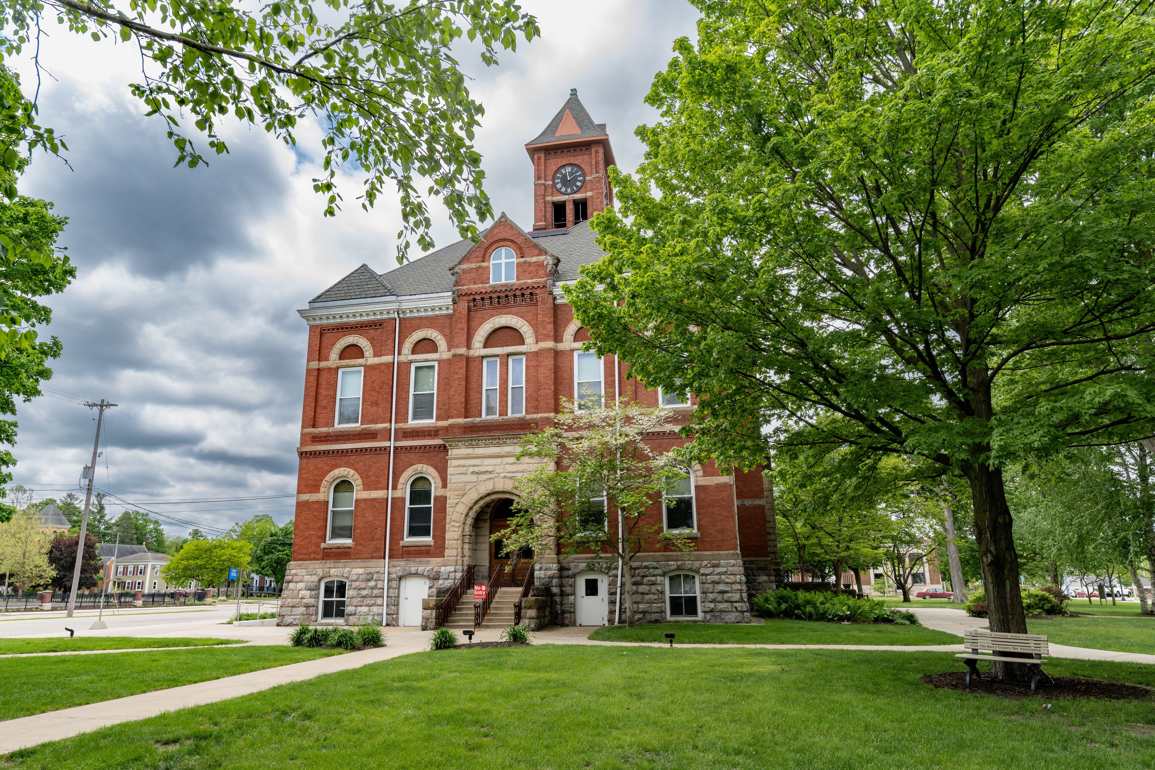 A historic red brick building with a clock tower, surrounded by lush green trees and a well-maintained lawn.