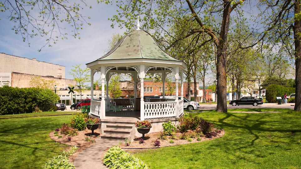 A gazebo surrounded by a garden with a brick building in the background.