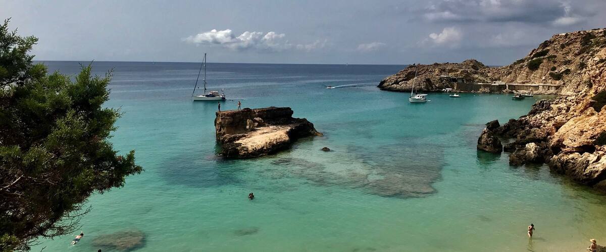 A coastal scene with clear turquoise waters, rocky outcrops, and boats anchored near the shore.