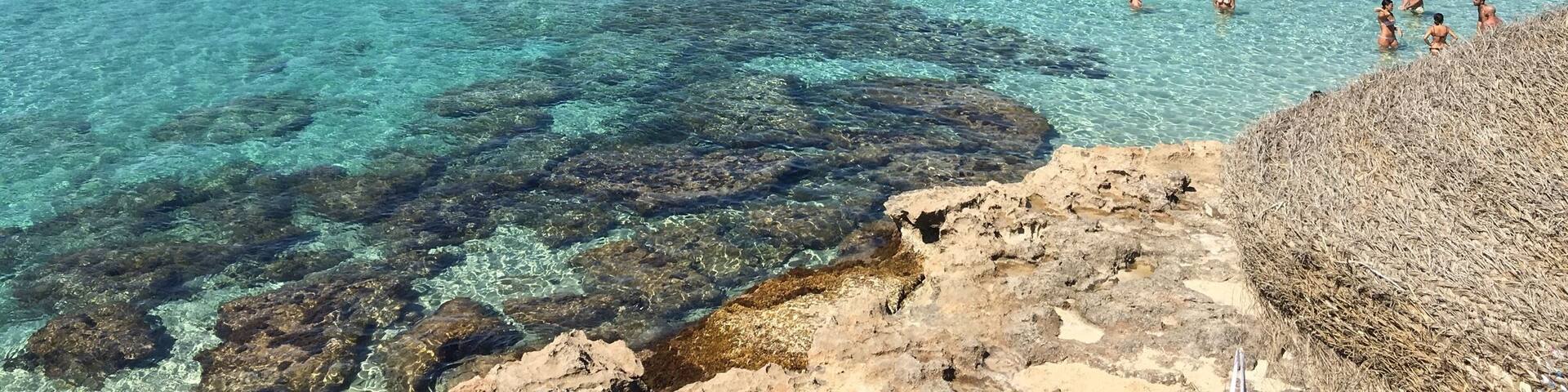 A clear blue sea with people swimming and a sailboat in the distance.