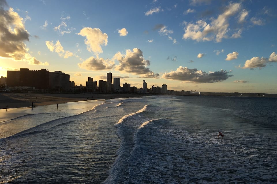 A beach with waves, a city skyline, and a bridge in the distance.