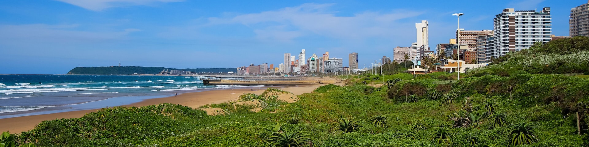 A coastal cityscape with a beach, dense greenery, and high-rise buildings.
