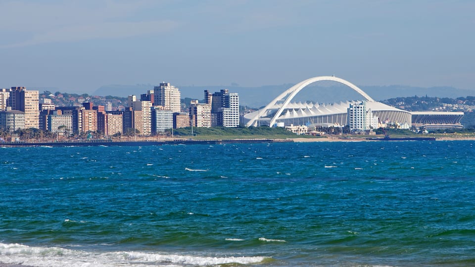 A coastal cityscape with a prominent white stadium and a dense cluster of high-rise buildings.
