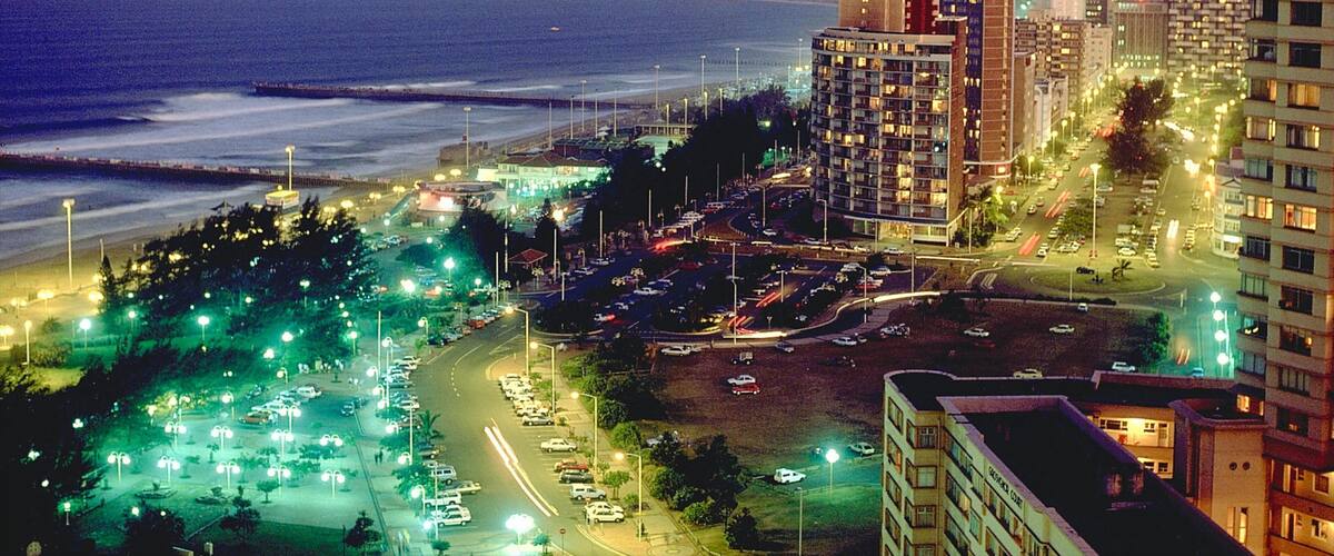 A coastal cityscape at night with a beach, high-rise buildings, and a busy parking area.