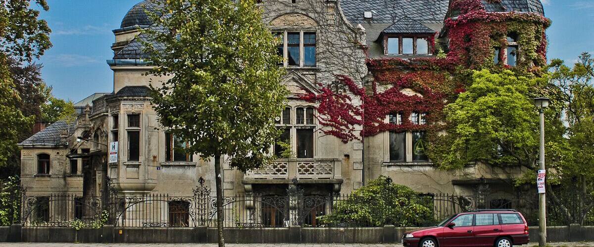 A historic stone building with a steeply pitched roof, ornate iron gates, and ivy-covered walls.