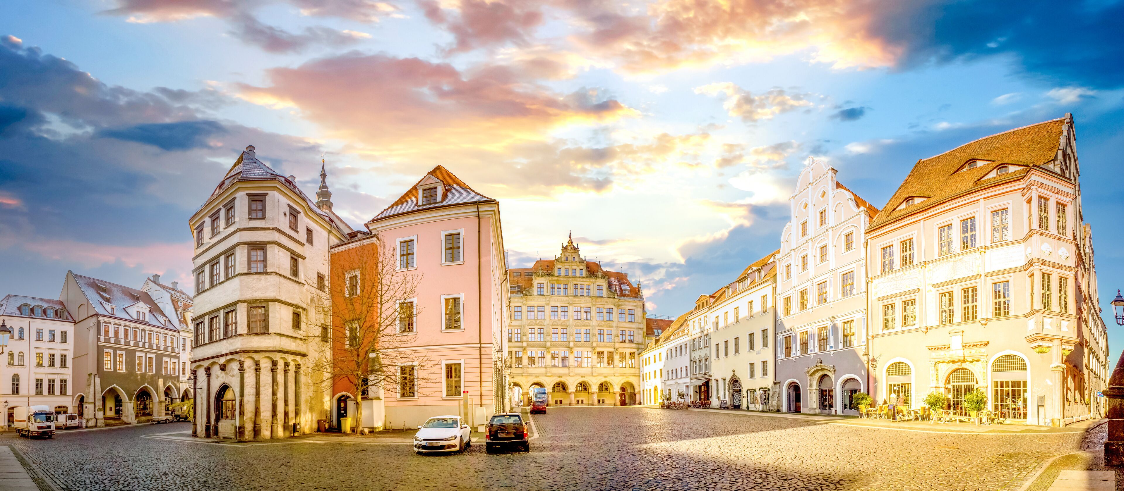 A cobblestone square with historic buildings, a church steeple, and a tram.