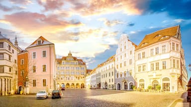 A cobblestone square with historic buildings, a church steeple, and a tram.
