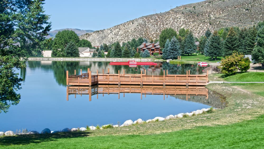 A calm lake with a wooden dock, surrounded by greenery and a mountain in the background.