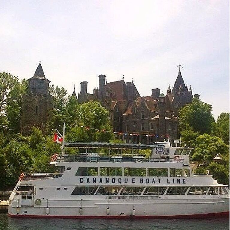 A white boat with "CANANOE BOAT LINE" written on the side, docked near a historic building with multiple spires.