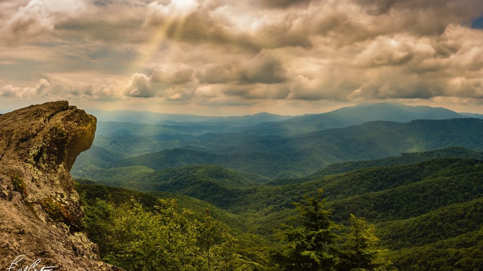 A mountain landscape with a prominent rock formation and dense forest.