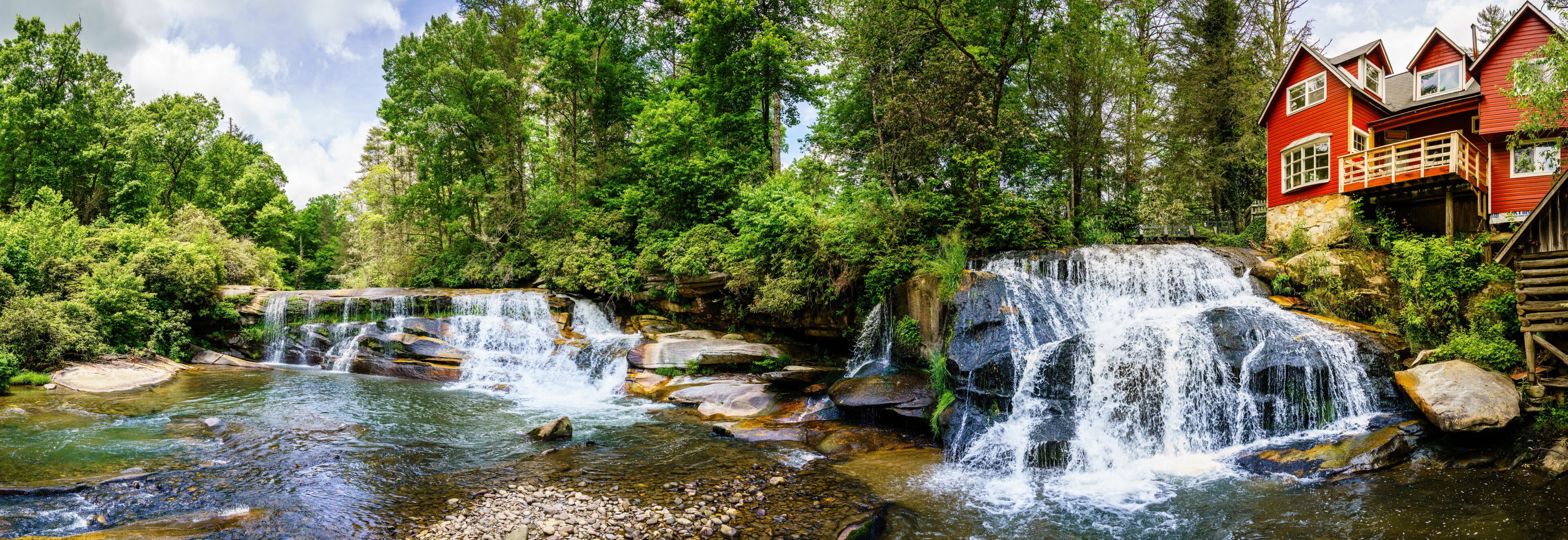 A waterfall, a river, and a red house with a wooden deck.