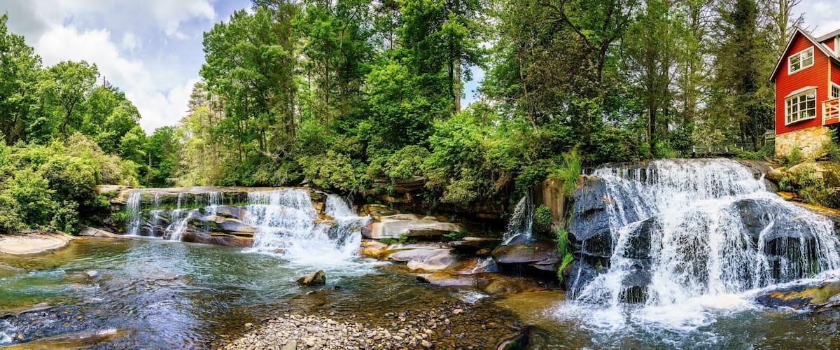A waterfall, a river, and a red house with a wooden deck.
