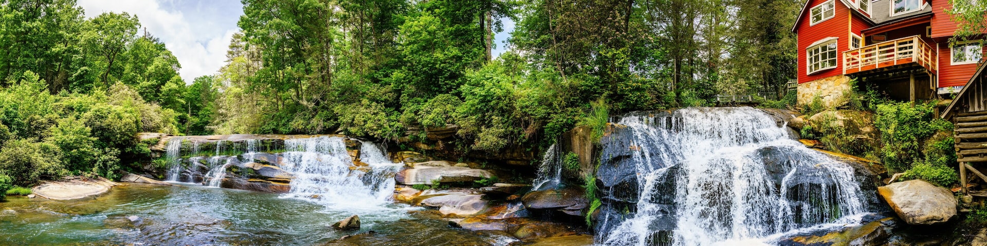A waterfall, a river, and a red house with a wooden deck.