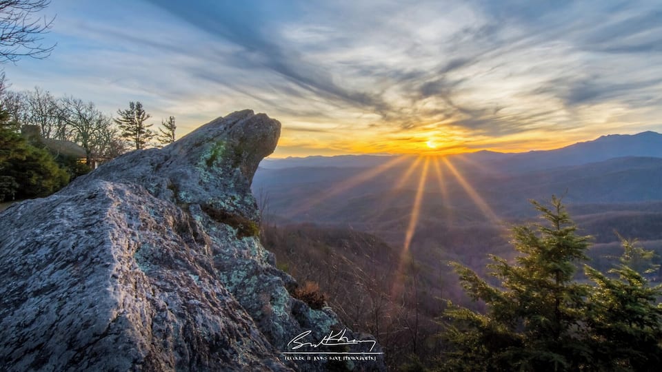 A rocky landscape with a sunrise or sunset, mountains in the background, and a clear sky.