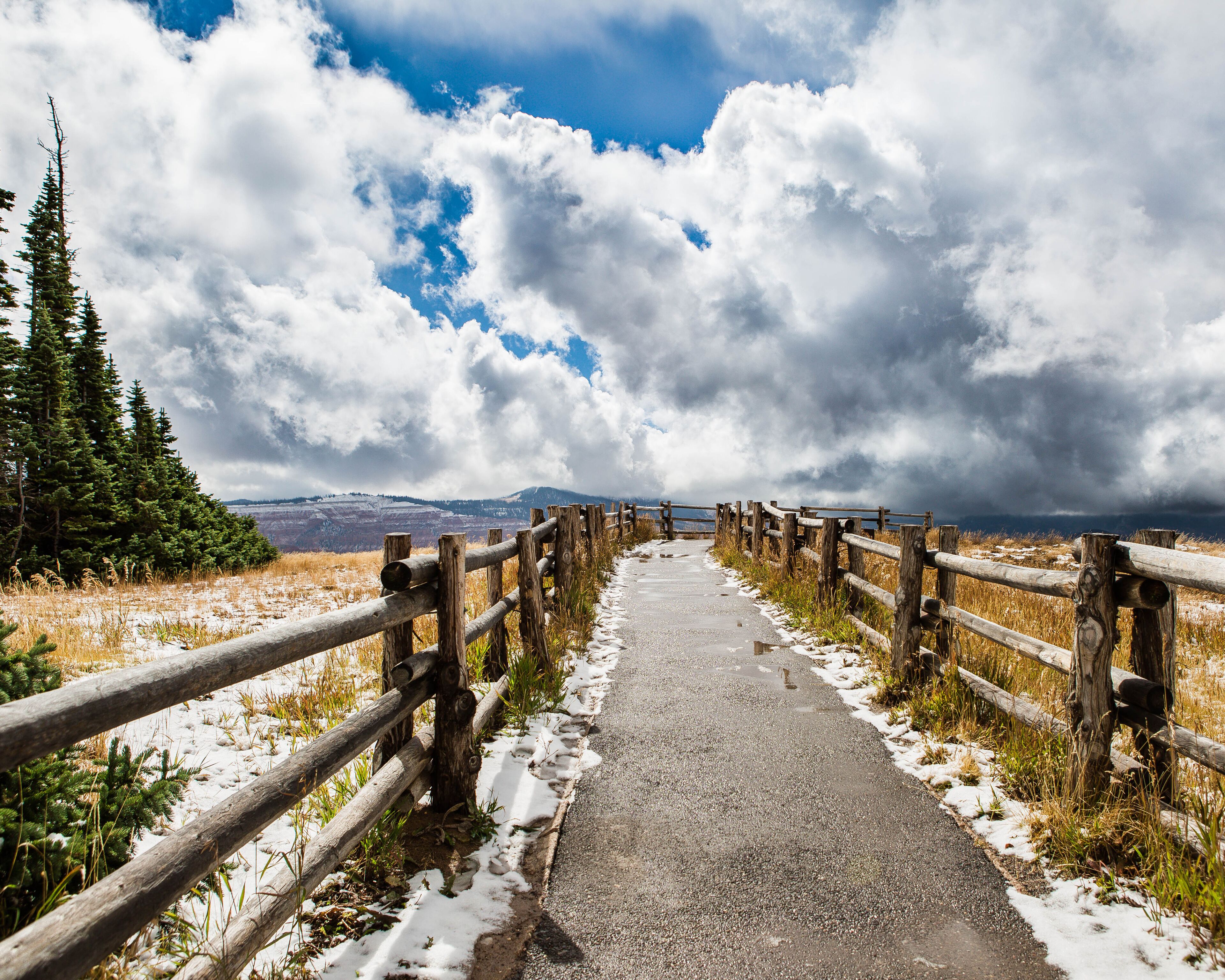 Trail in Brian Head Utah between rustic wood fence with snow, beautiful clouds & trees