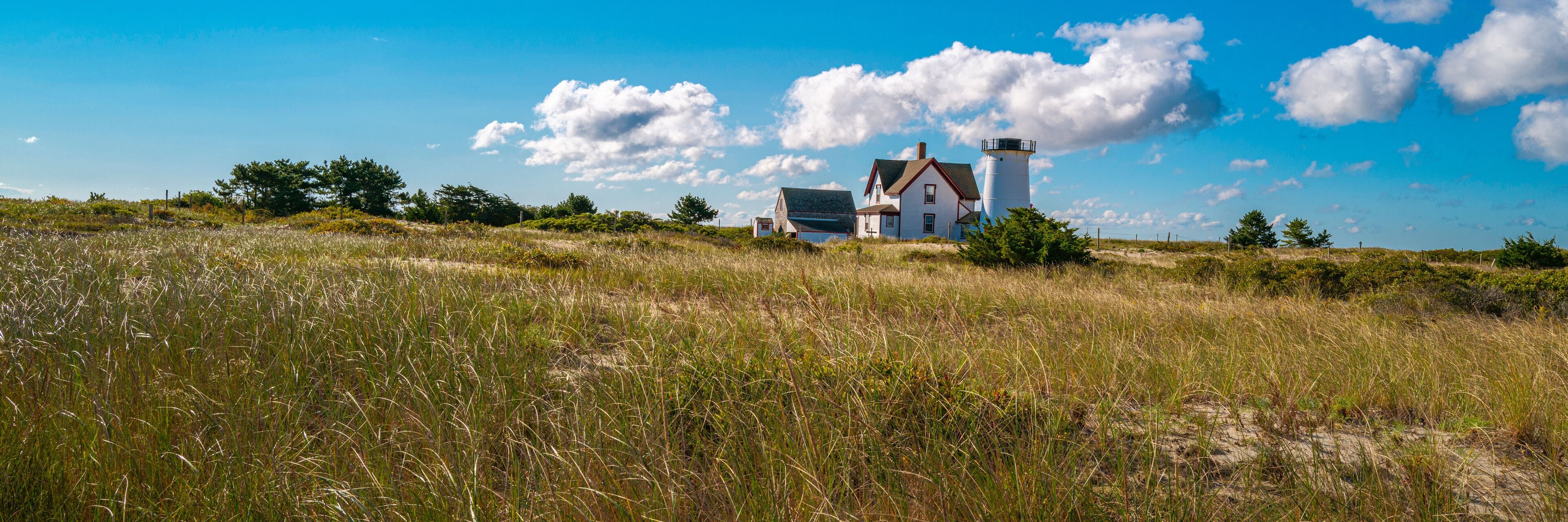 Panoramic autumn meadow landscape with the view of Stage Harbor Lighthouse under the white clouds floating in the blue sky
