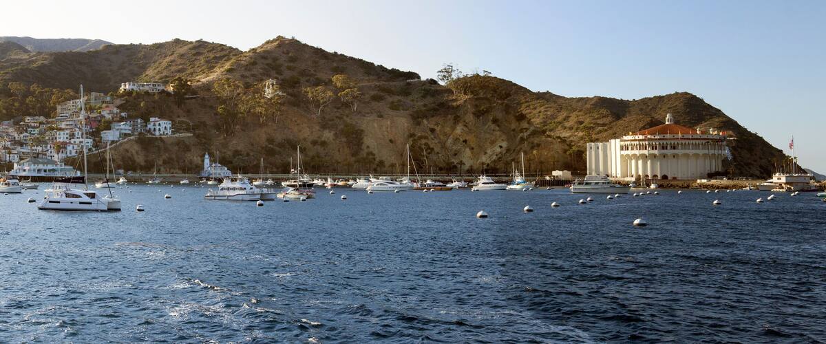 A coastal town with boats on the water, a large white building, and a hill in the background.
