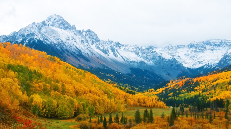 A mountainous landscape with autumn foliage and snow-capped peaks.