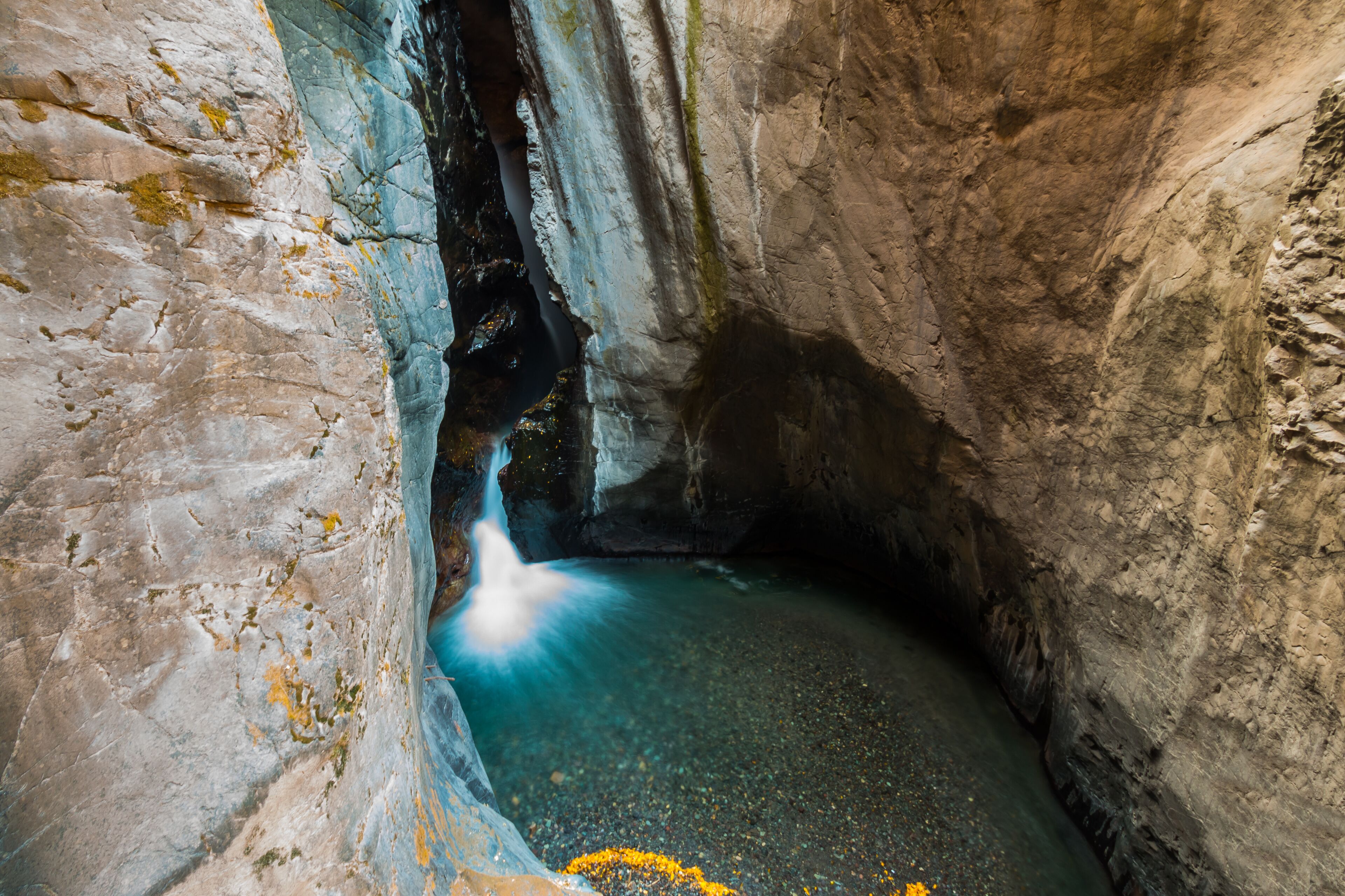 A cave with a water stream flowing through a narrow passage.