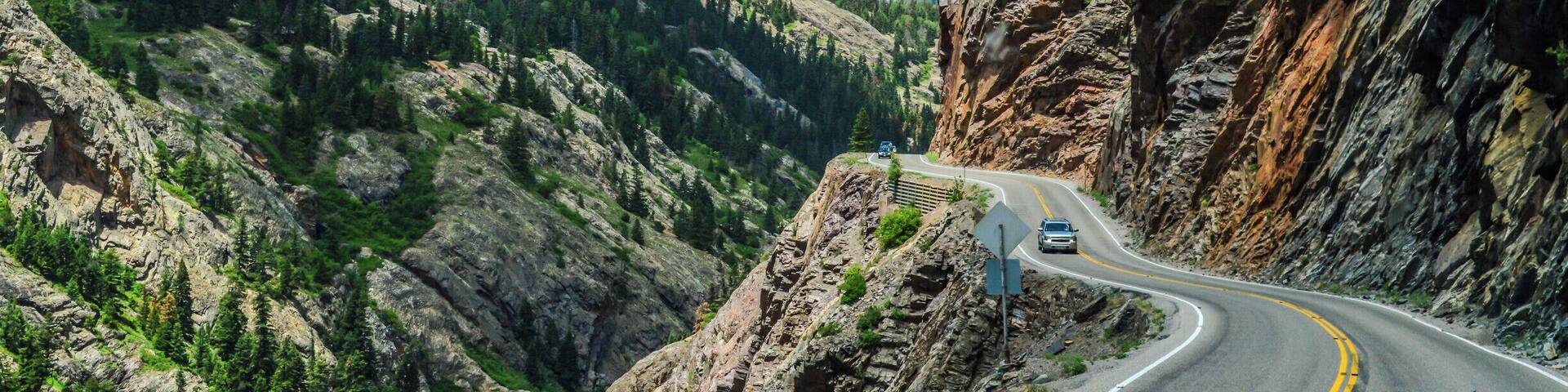 A winding mountain road with a car, surrounded by rocky cliffs and dense forests.
