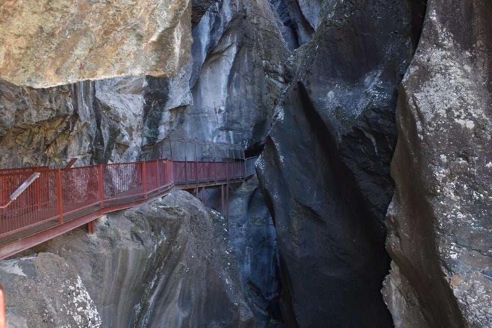 Un puente colgante rojo sobre un profundo desfiladero con paredes rocosas escarpadas.