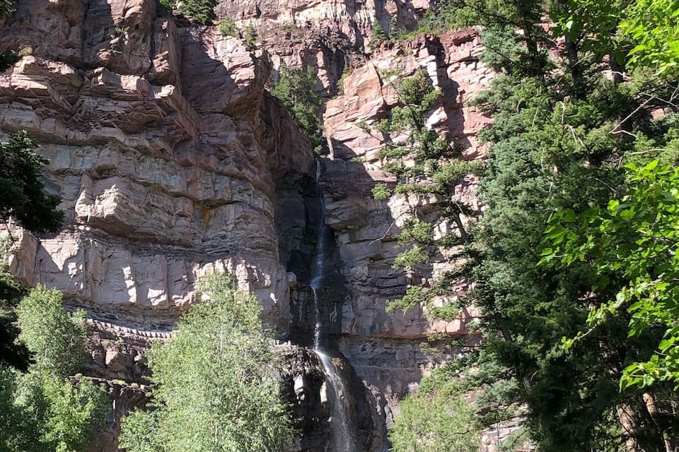 Una cascada se precipita por un risco rocoso rodeado de árboles.
