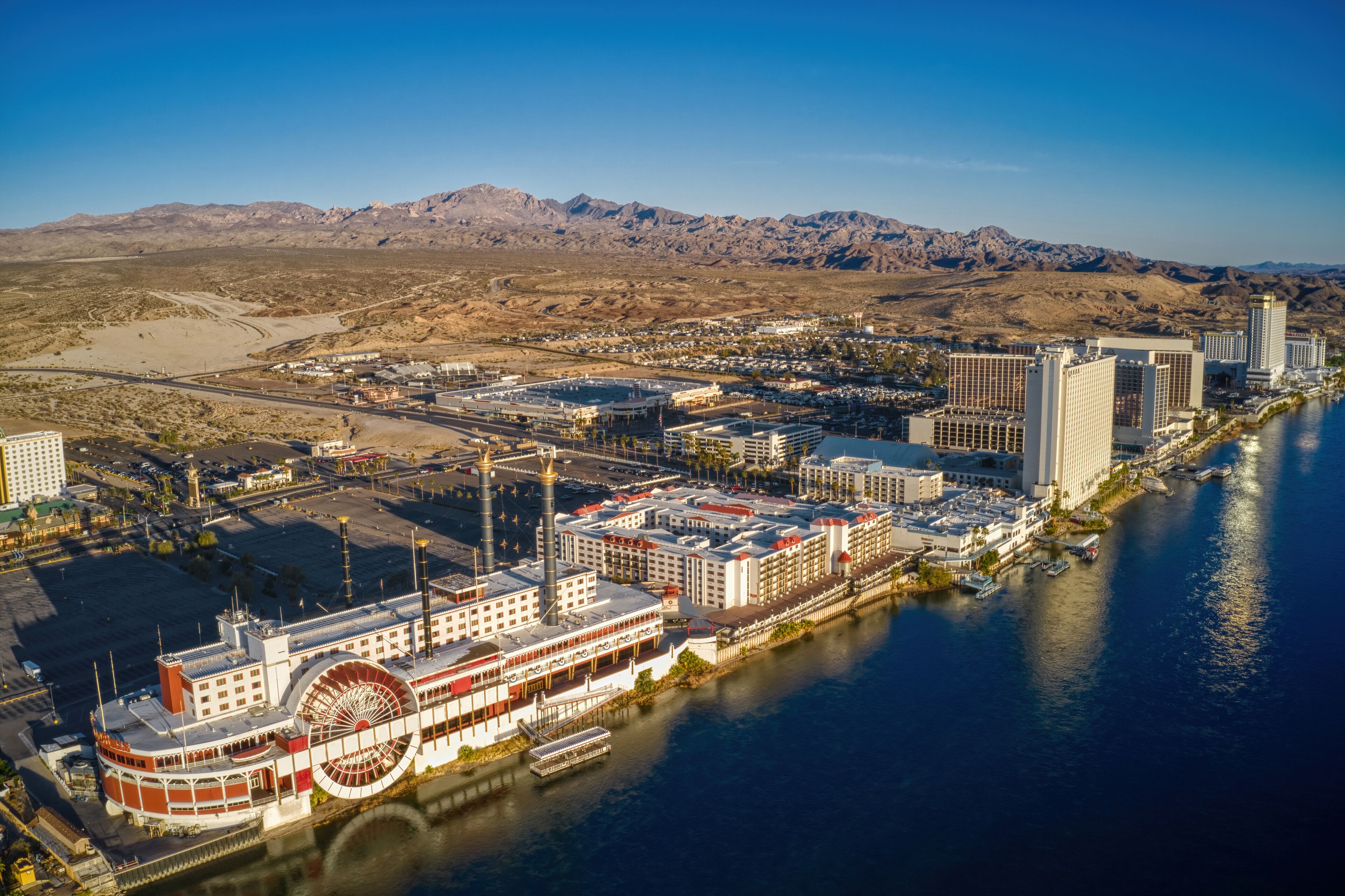 A riverfront cityscape with a prominent riverboat, high-rise buildings, and a mountainous backdrop.