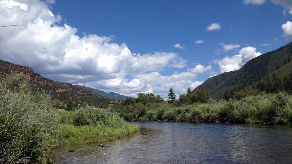A river flowing through a valley with mountains in the background and a clear blue sky.