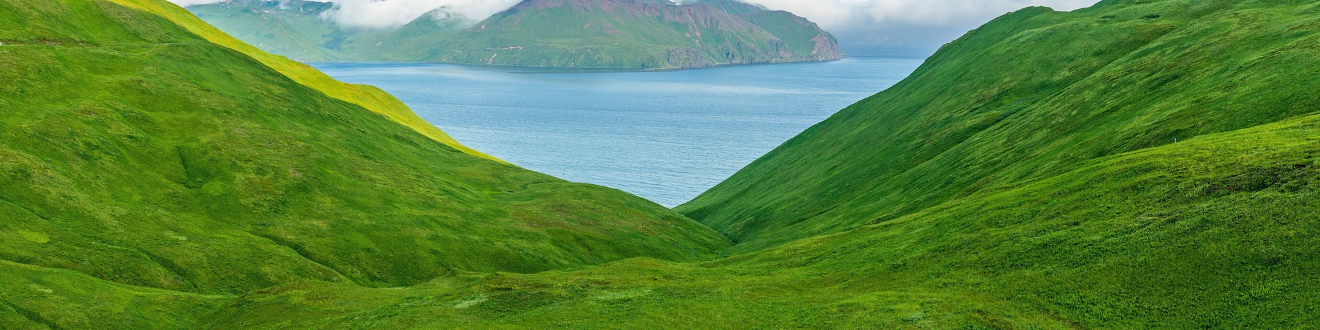 A green valley with a lake and a mountain in the background.