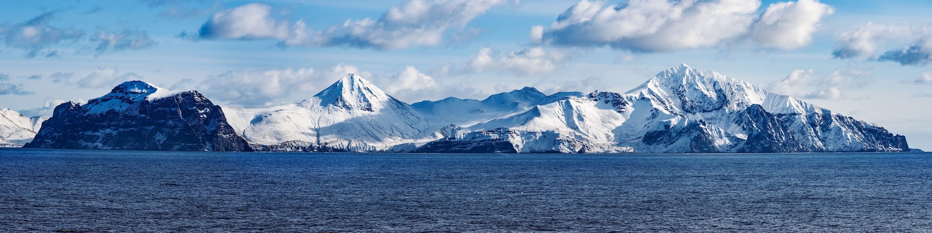 Snow peaks, glaciers and rocks of Aleutian islands in sunny winter day as viewed from ship passing in calm sea