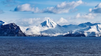 A glacier-covered mountain range with a body of water in the foreground.