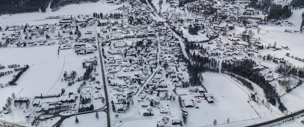 A snow-covered town with a winding road and dense forested mountains in the background.