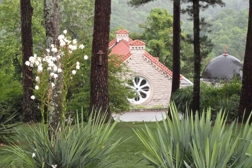 A garden with a stone house, a large white wheel, and a dome structure.