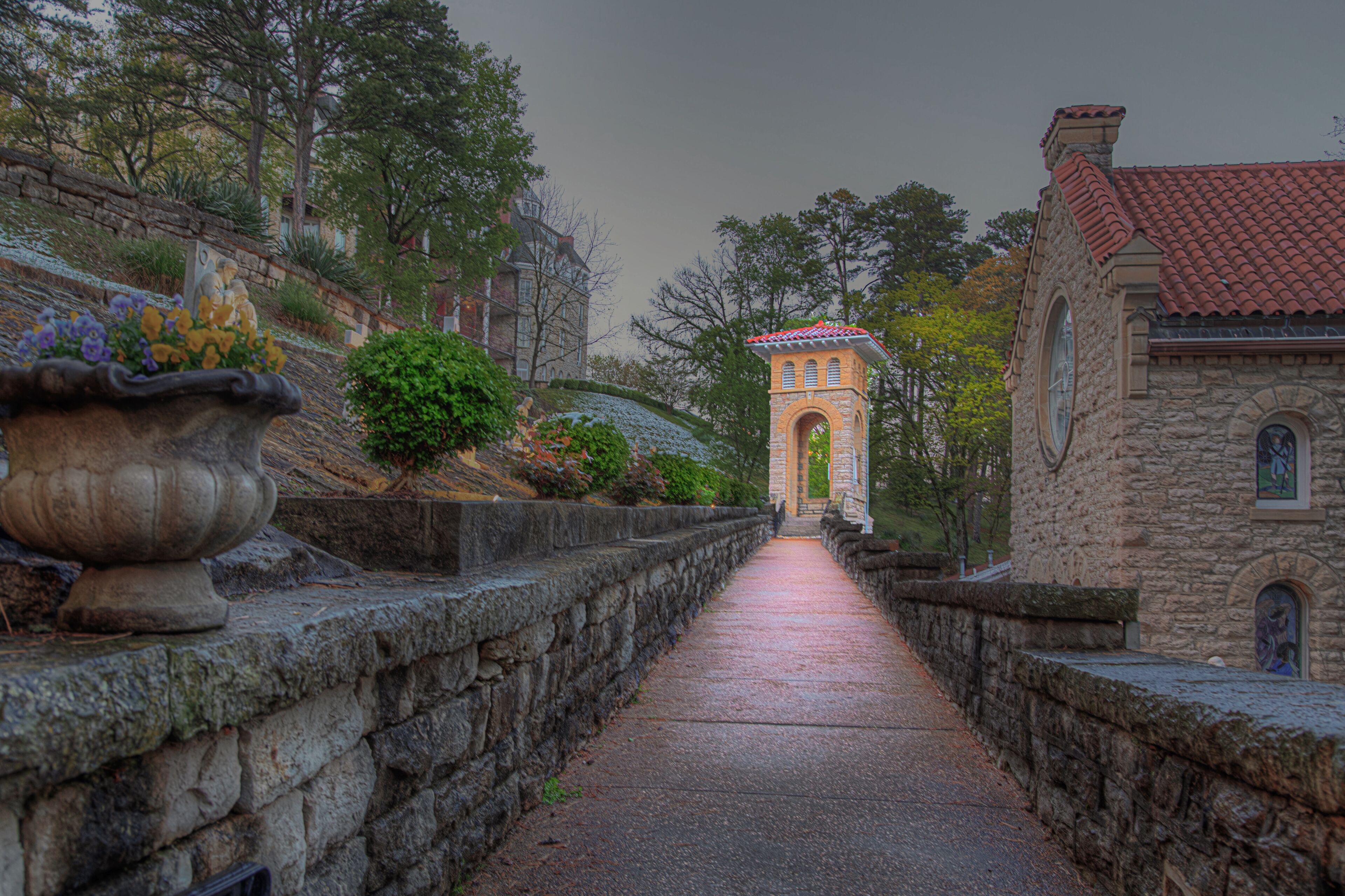 A stone pathway leading to a historic building with a red-tiled roof and an arched entrance.