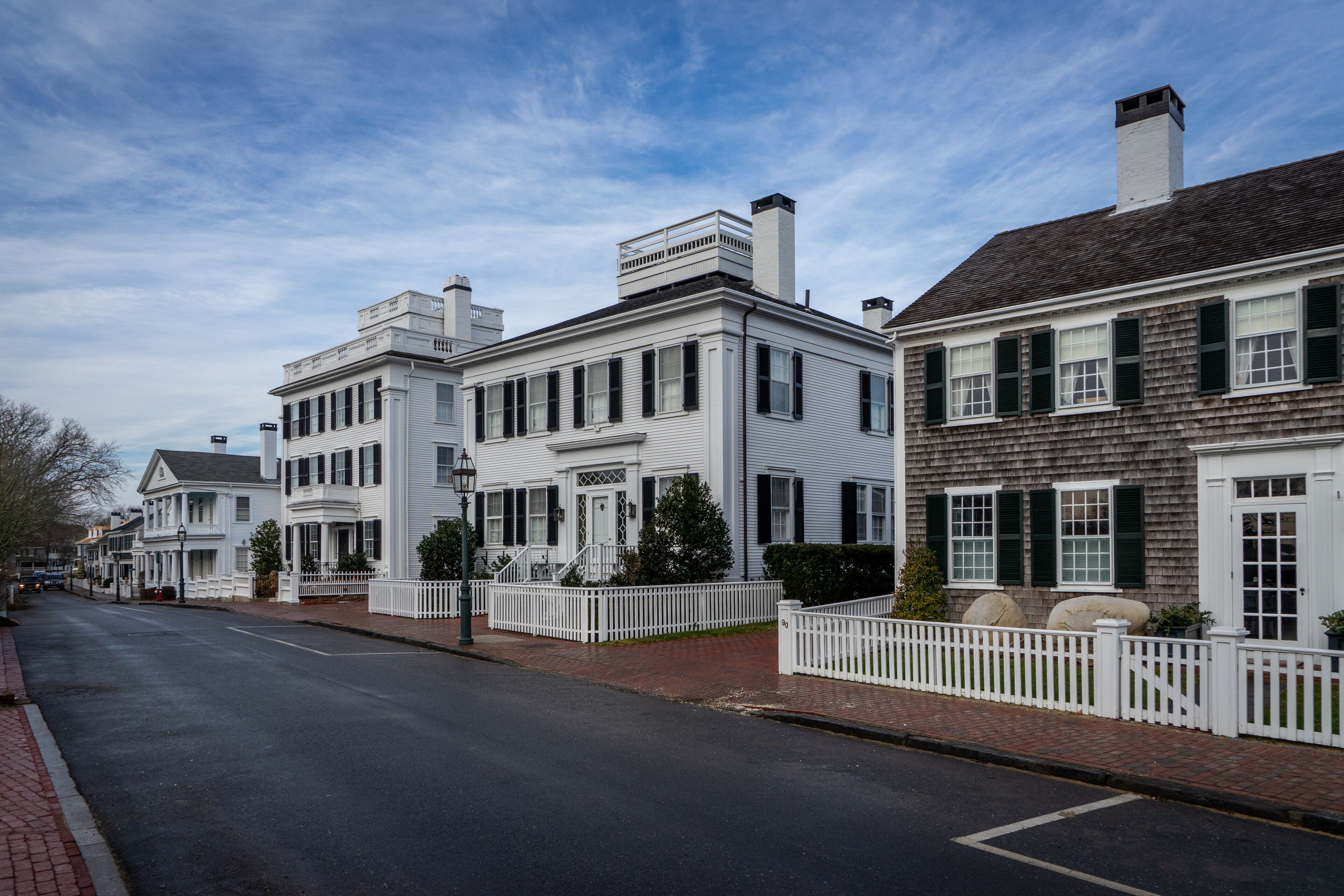 View of historic houses with white fences and black shutters along a quiet street on Martha's Vineyard in Edgartown, Massachusetts, United States.