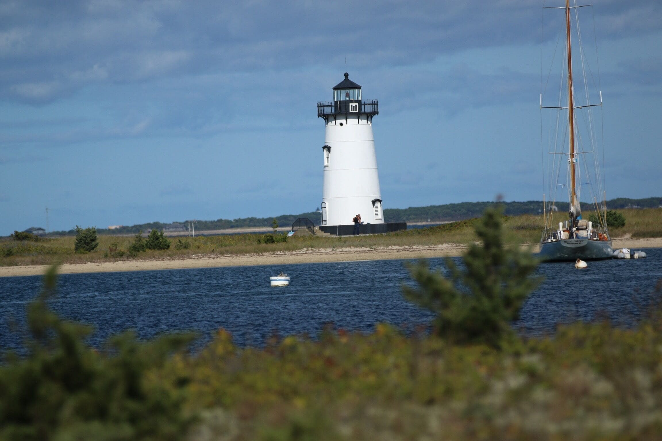 A lighthouse by the water with a sailboat nearby.