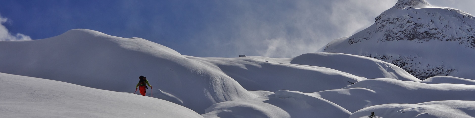 Un paisaje montañoso nevado con un alpinista y un pico destacado.