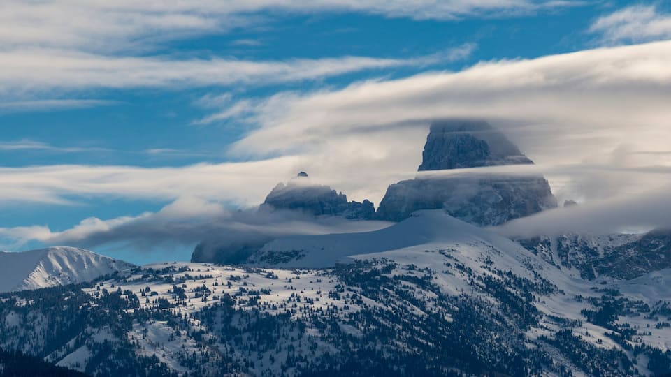 A snow-covered mountain range with a prominent peak and a cloud-covered sky.