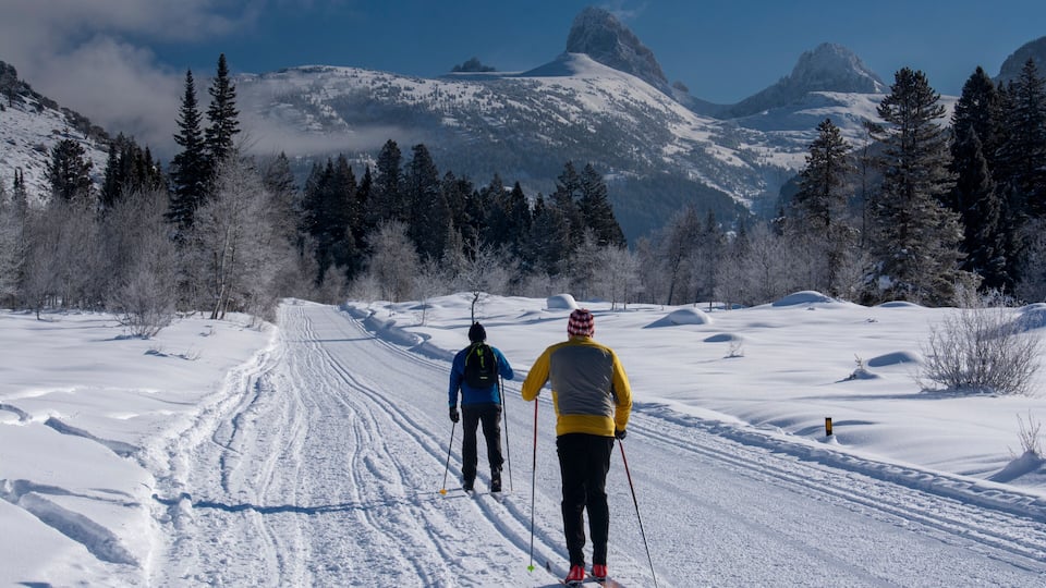 Two skiers on a snowy trail with mountains in the background.