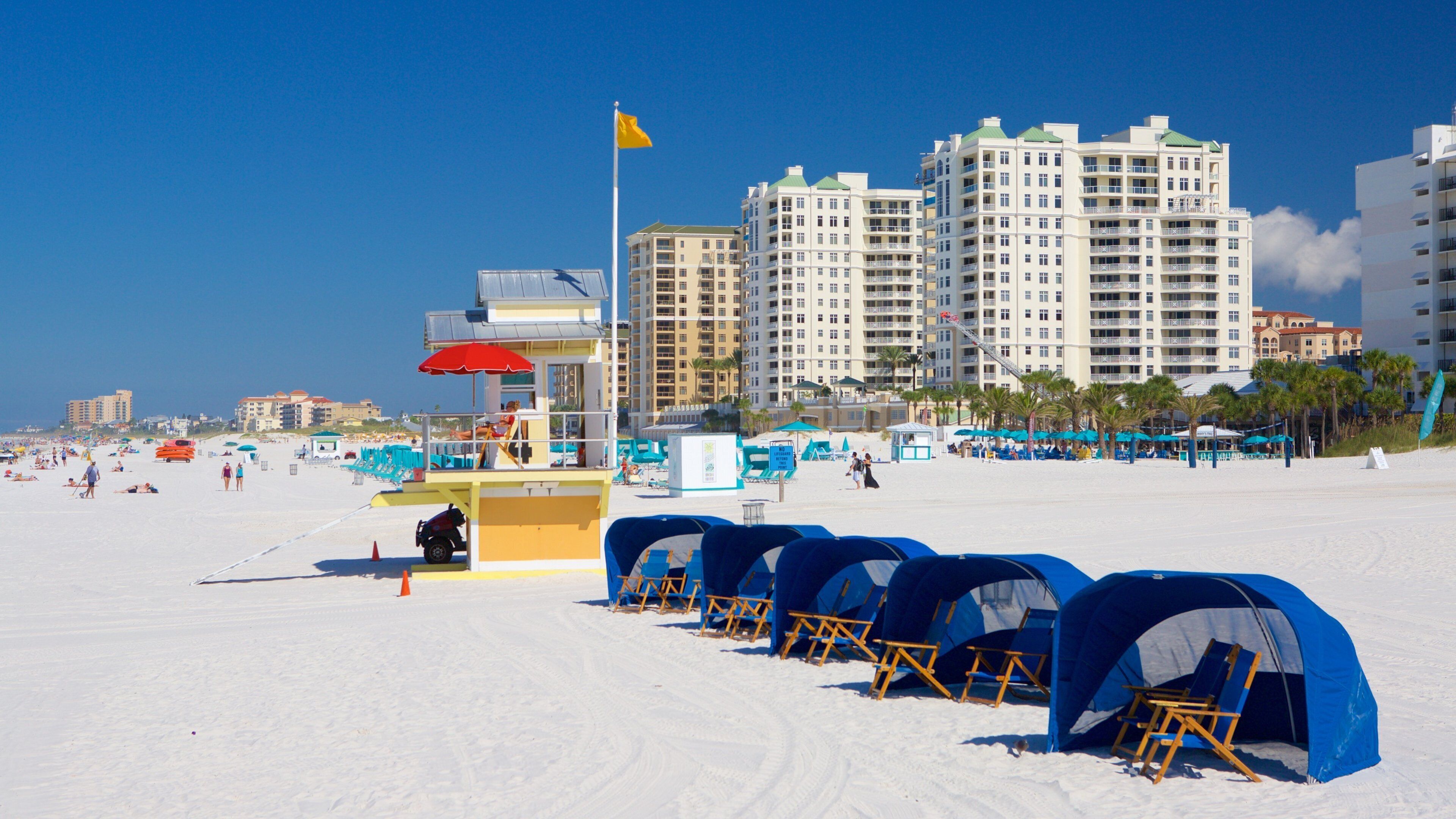 A beach with tents, a lifeguard tower, and high-rise buildings in the background.