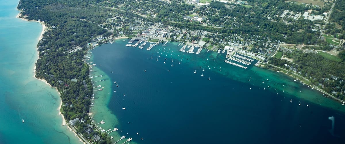 An aerial view of a coastal town with a marina, dense forested areas, and a beach.