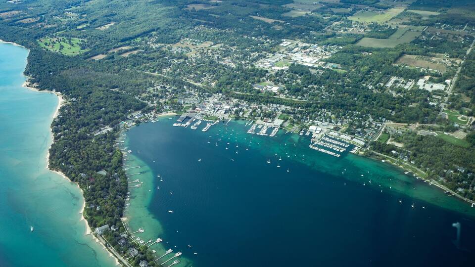 An aerial view of a coastal town with a marina, dense forested areas, and a beach.
