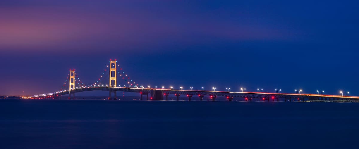 A long bridge with two towers, illuminated by lights against a twilight sky.