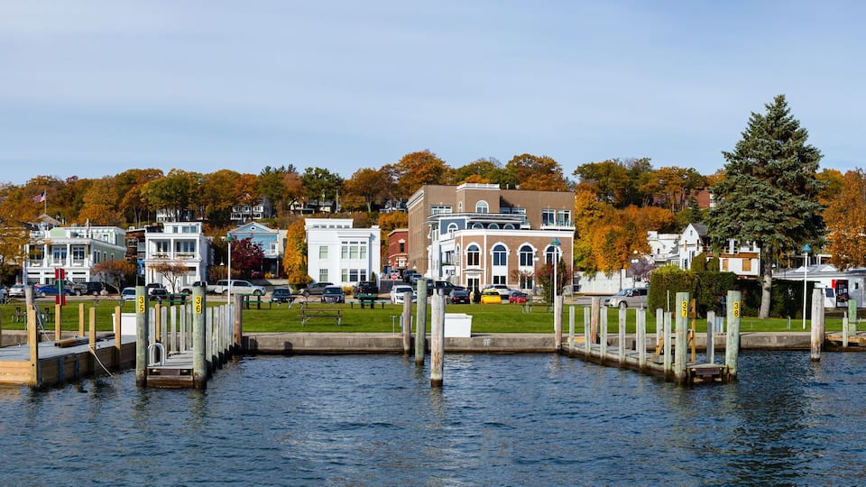 A waterfront with docks, a marina, and buildings with autumn foliage.