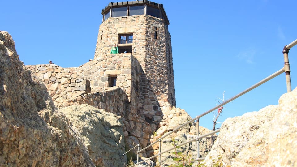 A stone tower with a balcony, surrounded by rocky terrain and a clear blue sky.