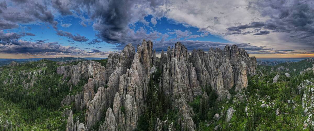 A rugged mountain landscape with tall, narrow rock formations and dense green forests.