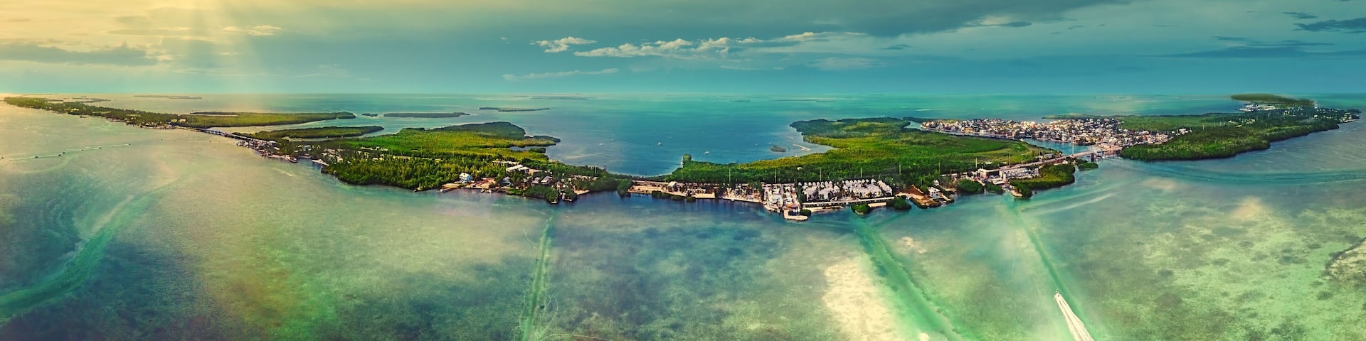 An aerial view of a coastal town with a marina, surrounded by clear blue waters and green islands.