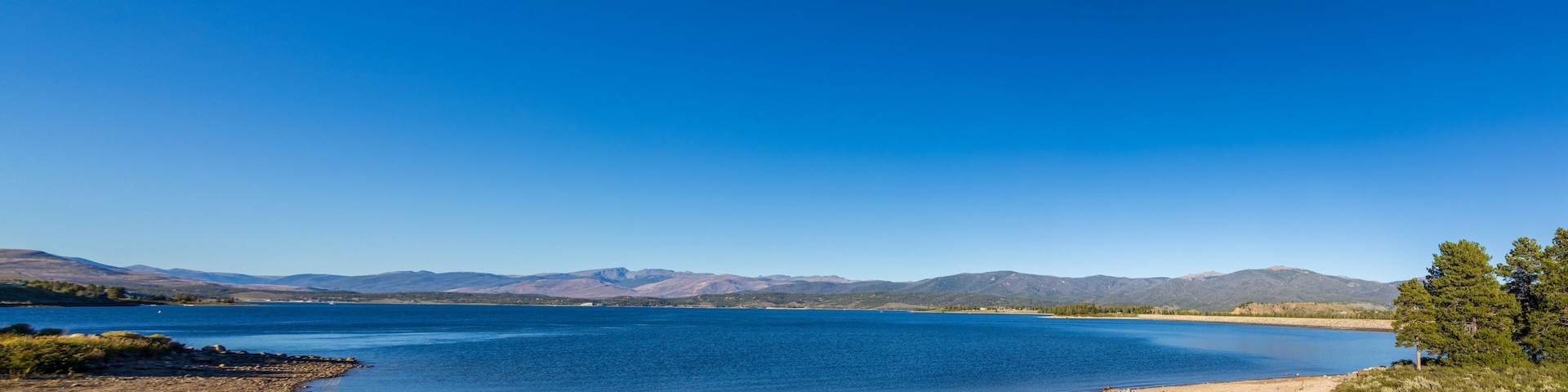 A large lake with clear blue water, surrounded by mountains and sparse vegetation.